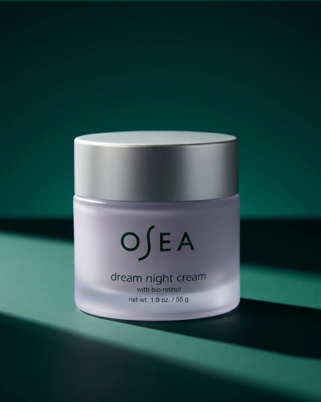 Frosted glass night-cream jar on dark green surface — AI skincare product photography for D2C beauty